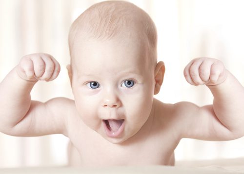 A baby with blue eyes and muscles in the air.