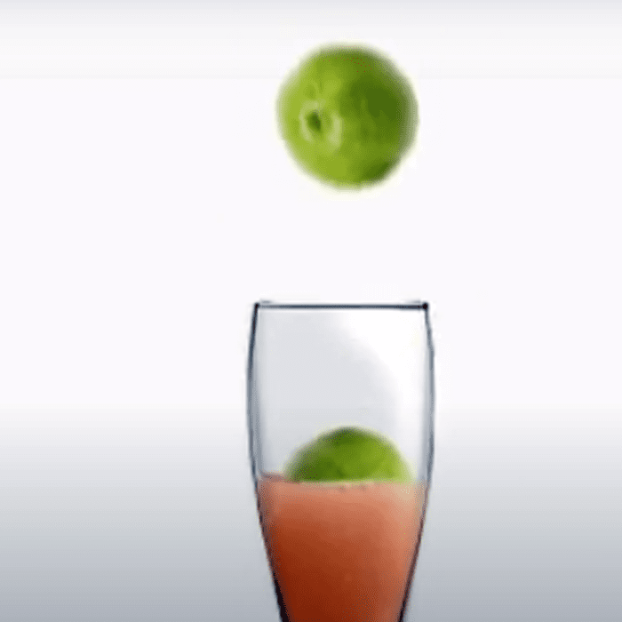 A glass of juice with an apple in the air.